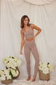 Woman wearing tan sports bra with matching yoga leggings between flowers