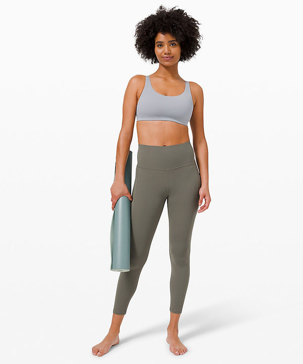 woman wearing a grey sports bra and grey sage yoga leggings carrying a yoga mat