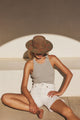 woman sitting down wearing a hat, grey tank top and white shorts