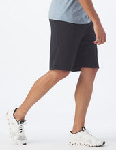 Load image into Gallery viewer, Man wearing black shorts from Glyder and white sneakers.