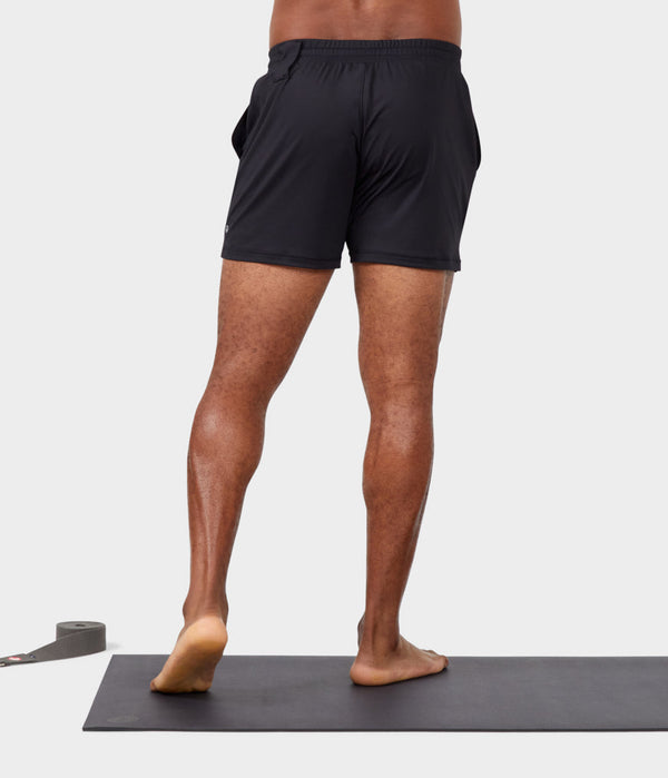 black male model standing on yoga mat wearing black athletic shorts