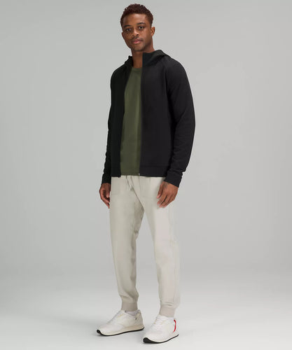Male model wearing full zip black hoodie with a green shirt and cream colored joggers
