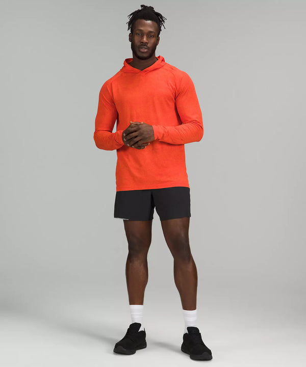 Black male model wearing black athletic shorts, black running shoes, and neon orange hoodie