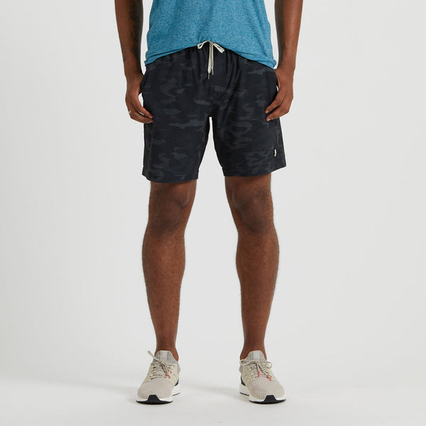 man wearing a blue tshirt with black camo vuori shorts and white sneakers