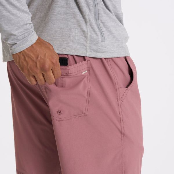 close up of a man opening the pocket of marsala vuori shorts and a grey shirt