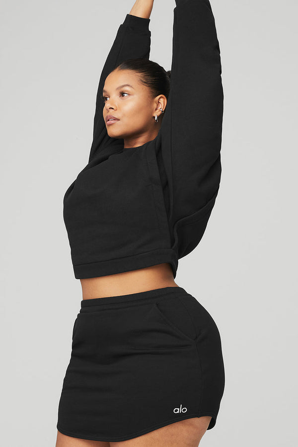 Black female model wearing black Alo Yoga pullover coverup and matching skirt
