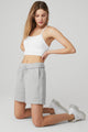 Female model wearing loose gray shorts and white tank from Alo Yoga 